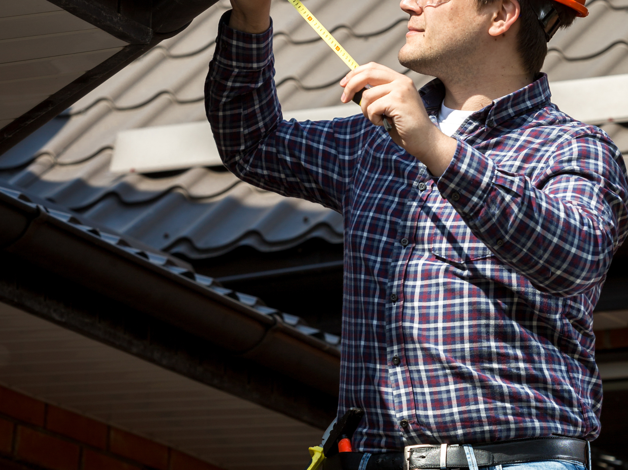 Person measuring a roof for a pergola installation with a tape measure