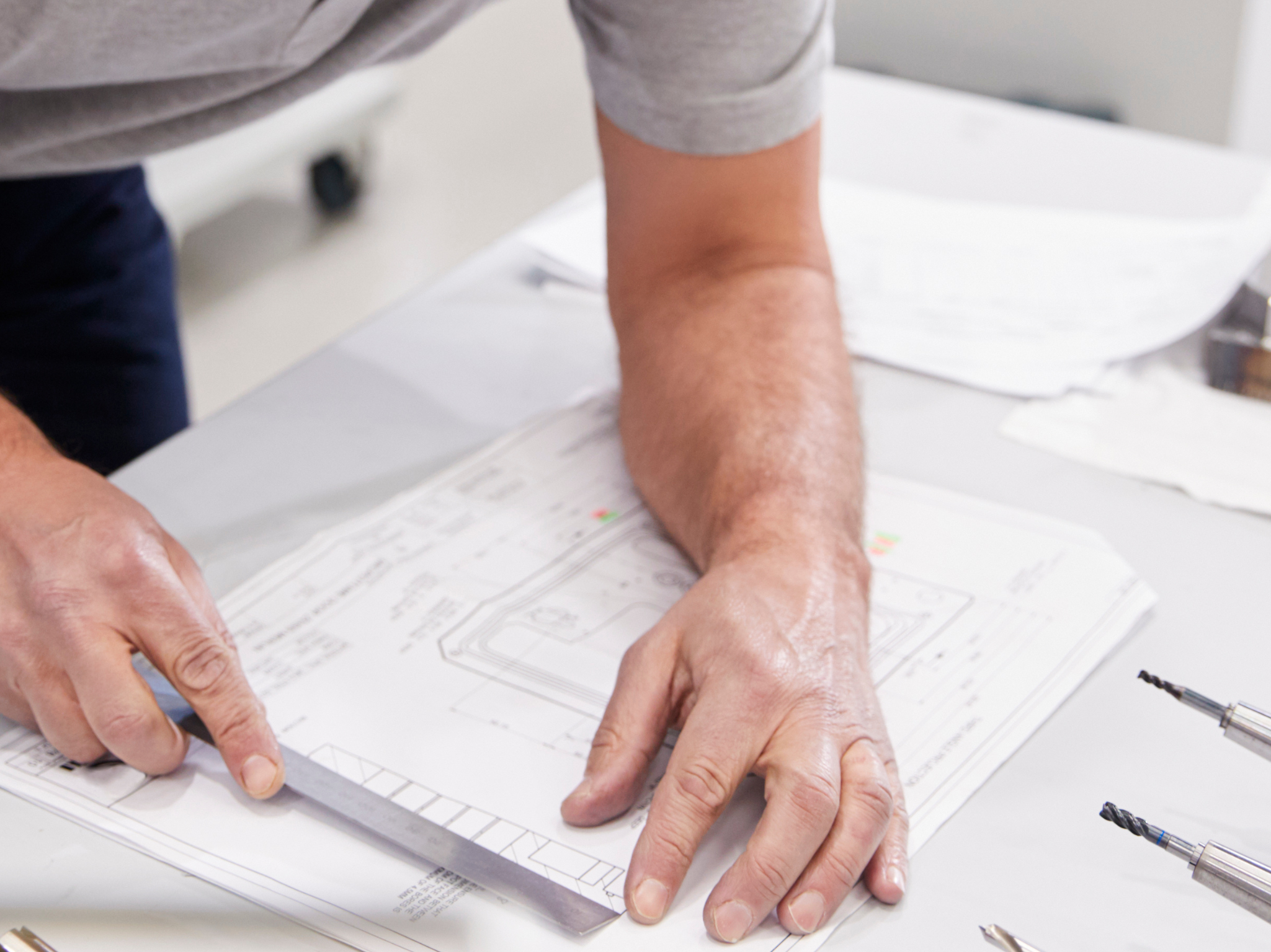 Person working on Moda Pergolas CAD drawings blueprints with tools on a table