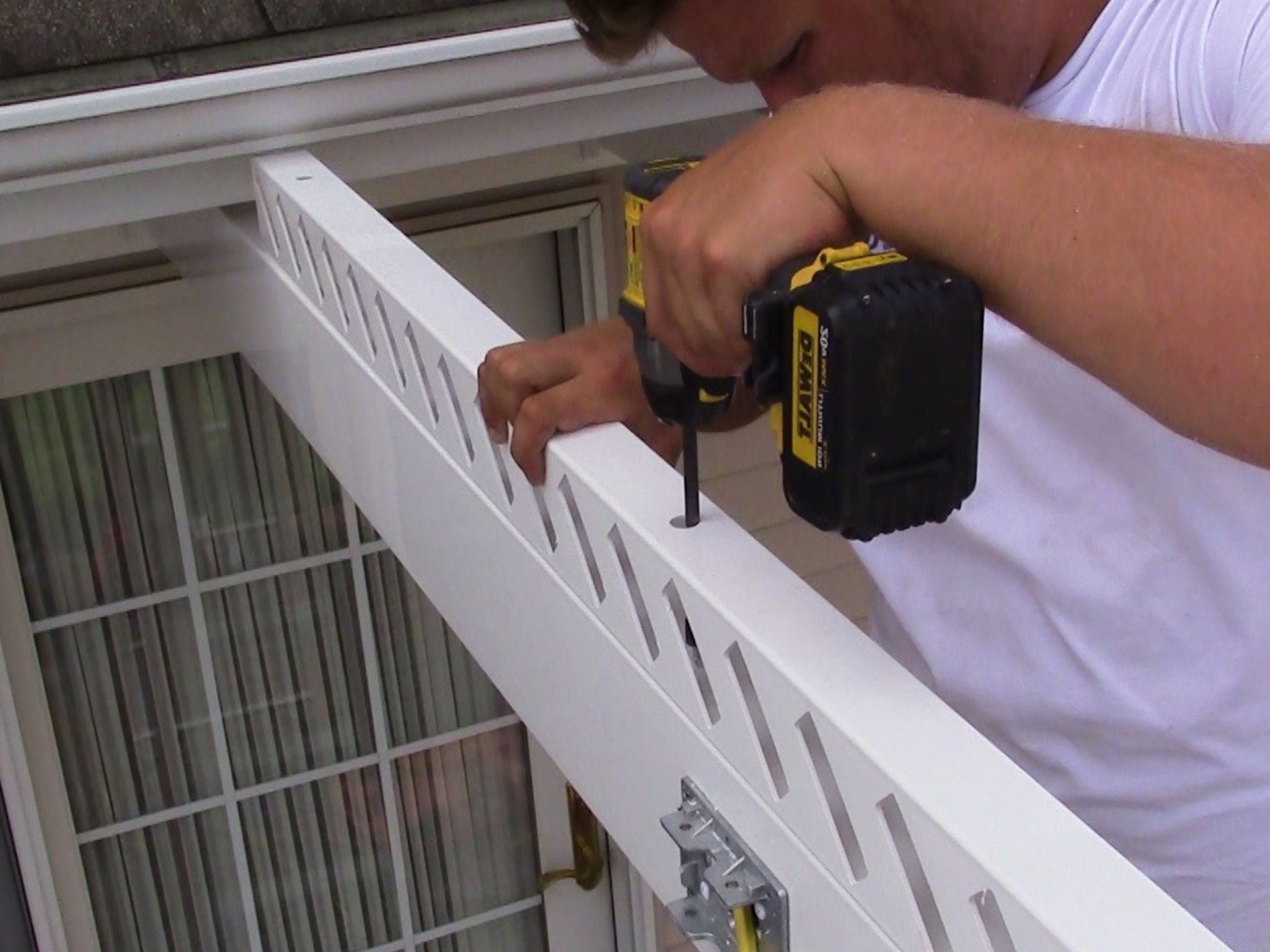 Person using a drill to install a pergola on a white railing with a window in the background