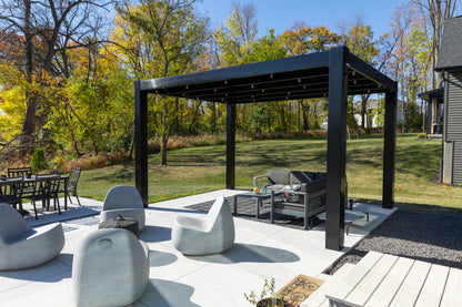 Outdoor patio with black modern pergola by Moda Pergolas, outdoor furniture, and trees in the background