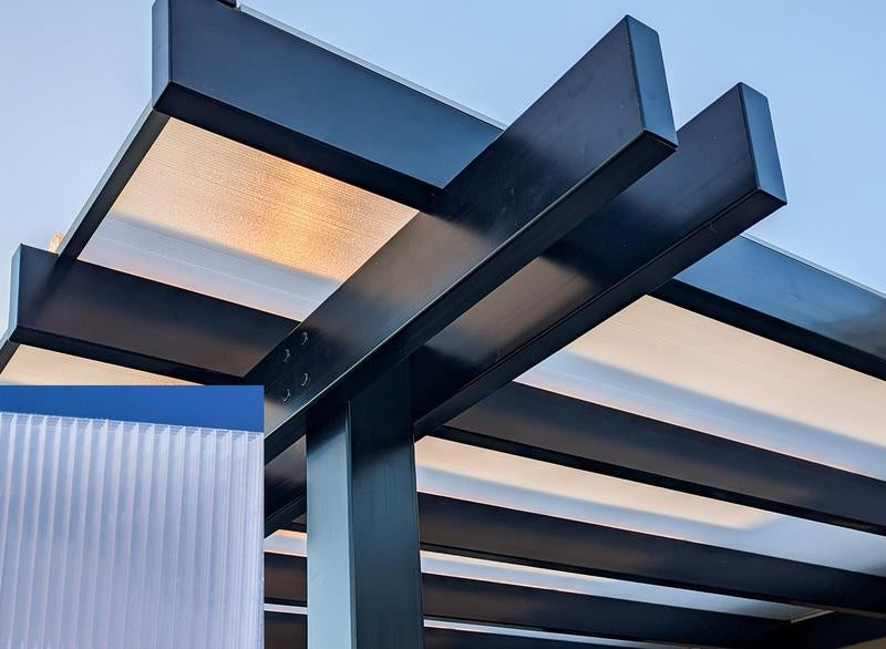 Modern covered pergola architectural design with beams and polycarbonate panels against a blue sky.